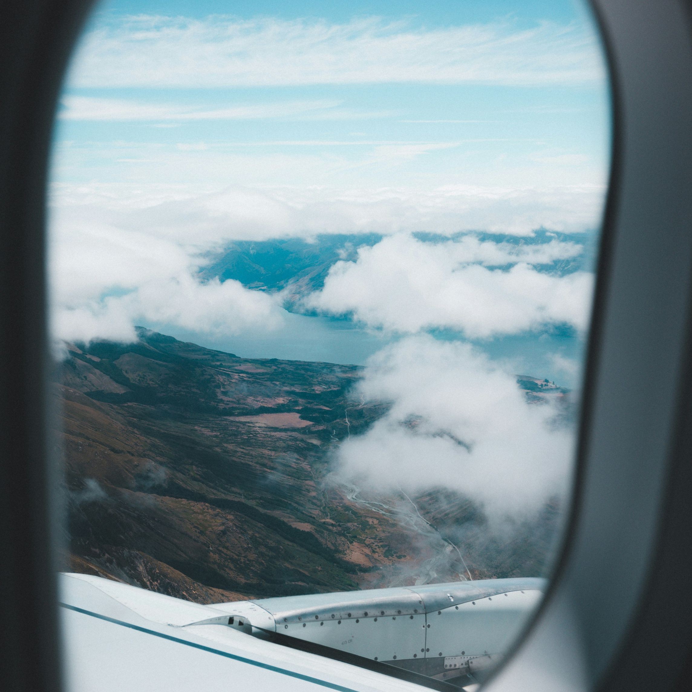 The view from an airplane window flying over mountains and a lake